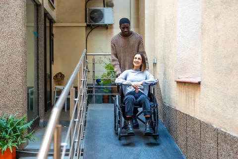 African man pushing the wheelchair of disabled colleague leaving a modern coworking building
