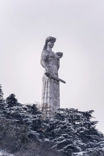 Majestic Mother of Georgia Statue amidst snow-covered trees in Tbilisi's historic center, capturing