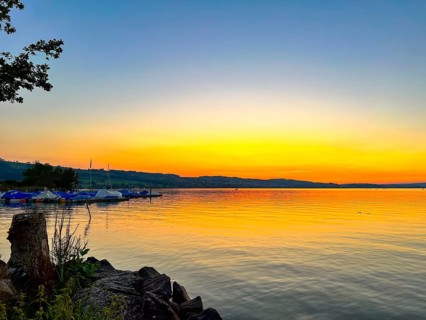 Lake Sempach at sunset with a bright, colourful sky and boats on the shore, Sempach, Lucerne,