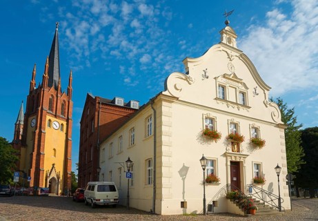 View of a church tower and a baroque building with a paved forecourt in sunny weather,
