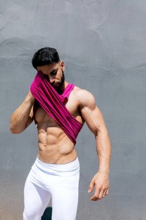 Fit man in white leggings and pink top wiping sweat from his face, standing against a textured