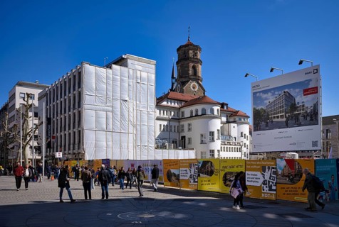 Construction site, construction fence, advertisement for DIBAG PATIO project, pedestrians,