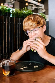 A young child wearing glasses enjoys a delicious hamburger at a cozy restaurant. The kid appears