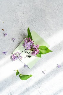 A pastel green envelope holds lilac flowers and a thank you card, elegantly positioned on a light
