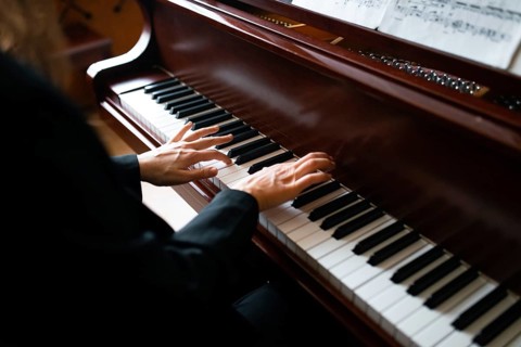 A skilled musician plays a grand piano, fingers gracefully dancing on the keys, while sheet music