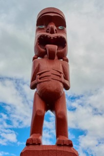 Red wooden figure of maori art with expressive face and hands on stomach, New Zealand Maori Arts