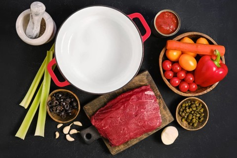 Preparing ingredients for a beef stew in a kitchen setting with fresh vegetables and meat