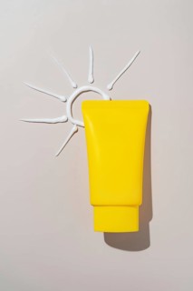 Yellow cosmetic tube on a pale surface with a sun shape created from cream. The textured background