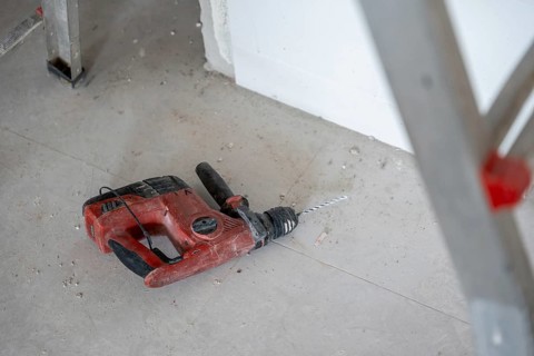 Rotary hammer drill lying on a dusty concrete floor in a room under renovation, indicating ongoing