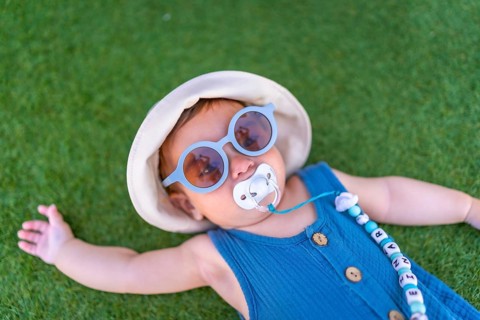 Top view of a baby girl with sunglasses and hat lying on grass next to swimming pool