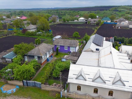 Overview of a rural settlement with solar panels on a large roof and small houses, contrasting rich