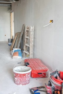 Empty room showing renovation progress with a dirty red bucket, toolbox, ladder, construction