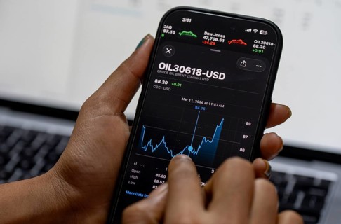 In this photo illustration, a person looks at a smartphone displaying Brent crude oil prices in