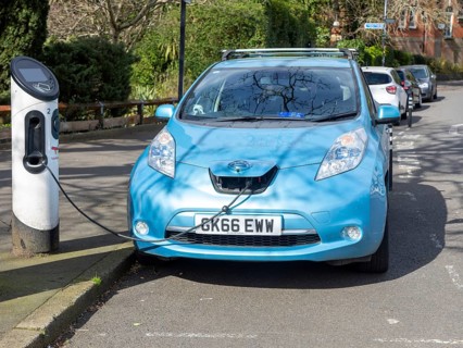 Nissan Leaf electric car connected to a white Char.gy bollard-style charger charging station,