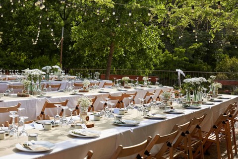 Beautiful boho wedding table setup outdoors featuring white floral arrangements in glass vases.