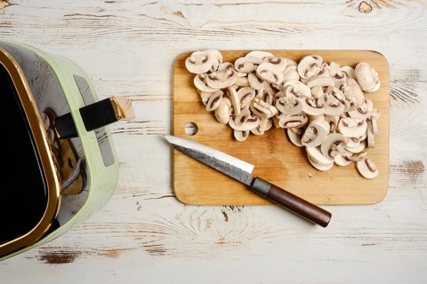 Cutting mushrooms next to air fryer on wooden surface in kitchen