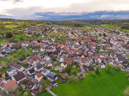 View of a village with scattered houses and green fields bordering a forest, Ostelsheim, district