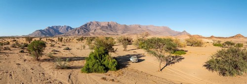 Aerial view of off-road car driving in dry riverbed and desert landscape on the Ugab River, behind