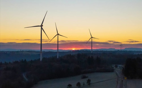 Wind turbines with a sunrise over a mountain landscape in the background, Rems Valley,