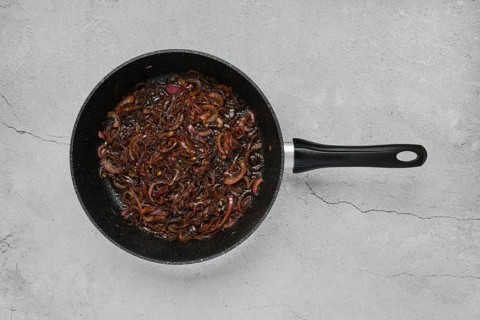 Caramelised onions are being sautéed in a black frying pan, turning rich brown while releasing