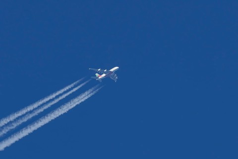 Airbus A380 jet passenger aircraft of Emirates airlines flying in a blue sky with contrails or