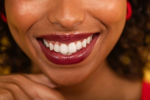 A close-up image of a bright, cheerful smile highlighted by vibrant red lipstick, showcasing white