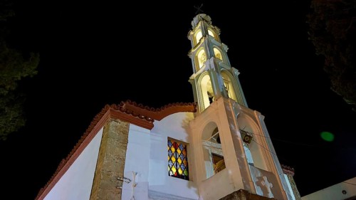 An illuminated church tower rises in the night, its architecture and the coloured windows radiate