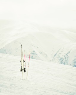 Pair of white skis with poles planted in snow on mountain slope with alpine peaks in background,
