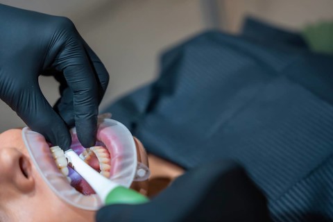 Dentist wearing black gloves uses a retractor and a special electric brush to whiten patient's