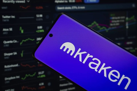 kraken logo is displayed on a smartphone screen, with a stock graph webpage visible on a computer