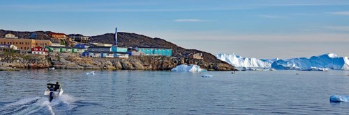 Coastal town with colorful buildings and boats, surrounded by icebergs and rocky landscape under