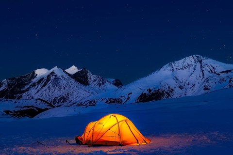 Illuminated tent in snow against snow-covered mountains and starry sky in Hidden Valley, plateau at