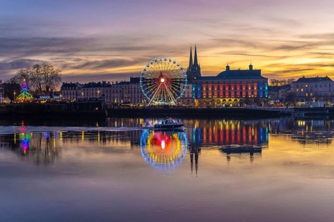 Bayonne cityscape illuminating the adour river with colorful christmas lights, a ferris wheel, and