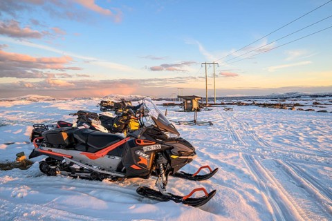 Several snowmobiles are standing in a snowy landscape under clear skies, ready for an adventure,