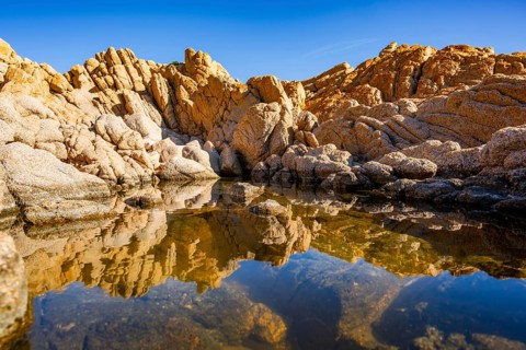 Reflection of stones in a puddle of water from the rocks on the beach at Marinedda Coast on a sunny