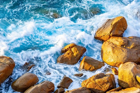 Surf at the coastline, blue water flows around the stones at Costa Paradiso in eveneing light,