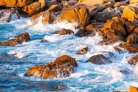 Surf at the coastline, blue water flows around the stones at Costa Paradiso in eveneing light,