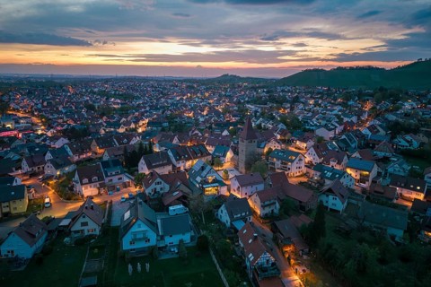 City view at dusk with illuminated houses and a church under a picturesque evening sky, Korb im