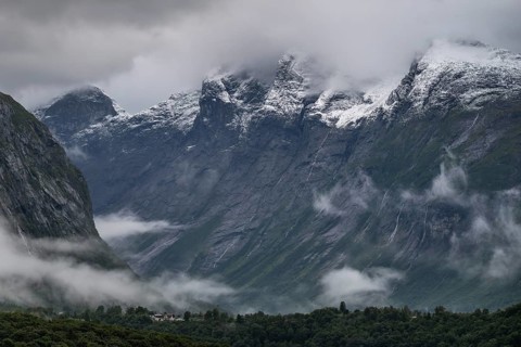 Freshly snow-covered mountain range above a valley and low-hanging scraps of clouds on the valley