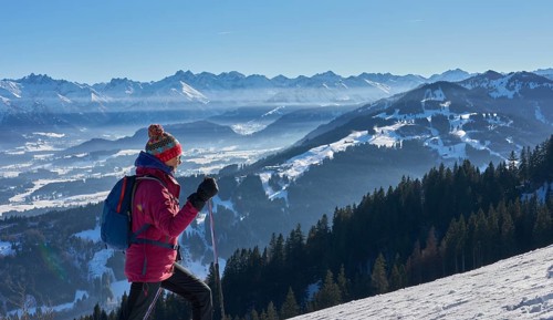 Nice and active senior woman snowshoeing in in the snow covered Allgaue alps above the valley of