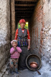 Friendly young woman in traditional dress with toddler in a covered doorway, Tangge, Mustang, Upper