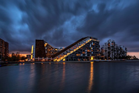Modernes Gebäude bei Nacht mit dramatischem Himmel und beleuchteten Fenstern am Wasser, Kopenhagen,