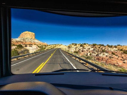 Vehicle driver's perspective traveling on a winding highway through a vast desert landscape,