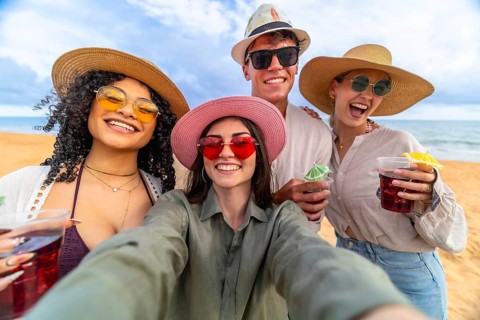 Group of diverse young happy friends laughing and smiling while taking a selfie on a sandy beach,