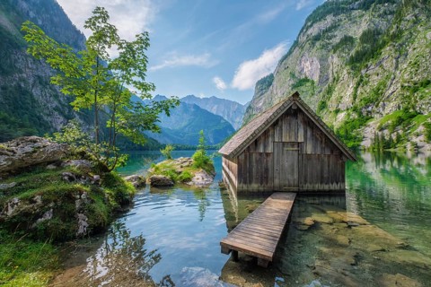 Vibrant summer landscape of the boathouse at Obersee lake with green trees and crystal clear