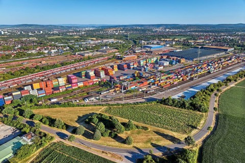 Aerial view of a large container terminal with freight trains, shipping containers, cranes, and