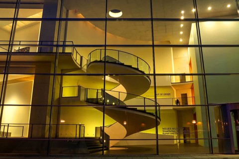 View through the glass façade into the stairwell of the State Museum of Art and Design in evening