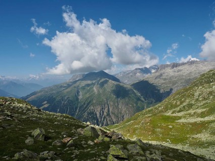 Impressive mountain range under a blue sky with white clouds. Green slopes lead into the distance,