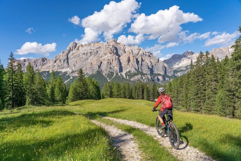 Woman cycling with electric mountain bike below the spectacular summits of Fanes Group, Dolomites,