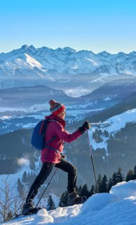 Sportive senior woman hiking with snow shoes in the snowy Allgaeu Alps above Lake Alosee,